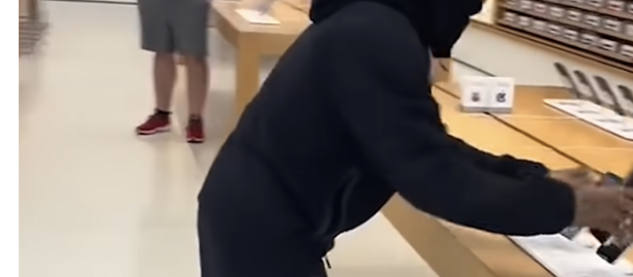 Thief carrying stolen iPhones from an Apple Store while a police car is parked outside